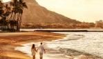 Photo of a happy young couple walking hand-in-hand on Waikiki beach at sunrise.