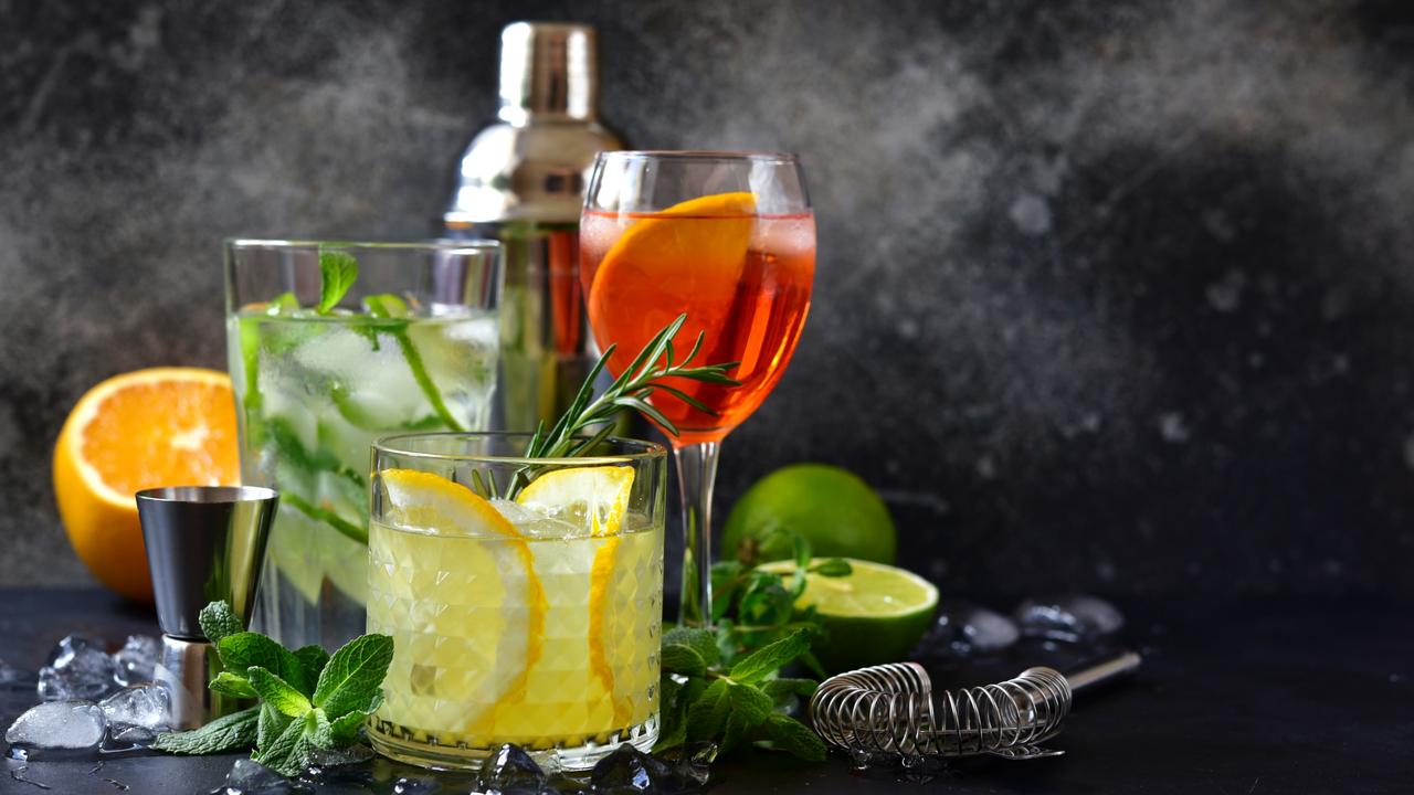 Three classic cocktails : aperol spritz, mojito and lemon cooler with rosemary with ingredients for making and cocktail set on a dark slate, stone or concrete background.