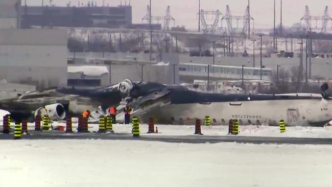 This image taken from video provided by CTV shows workers near the crashed passenger jet on a tarmac of the Toronto Pearson Airport. Picture: CTV via AP