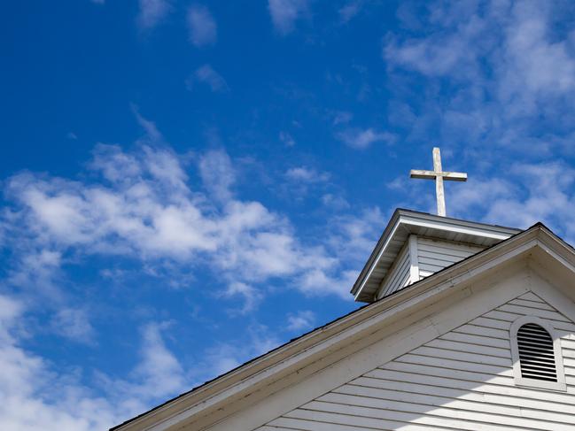 Wooden cross on a simple steeple set against a sunny summer blue sky.