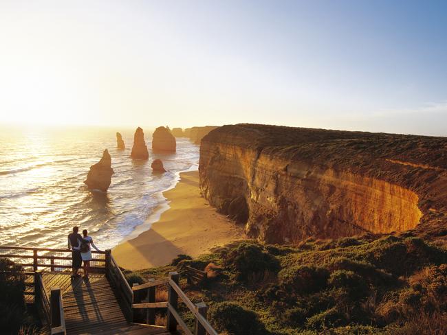 Man and woman admiring the sea at sunset.  In the distance are the Twelve Apostles, unique rock formations that rise out of the sea along the Victorian coast. Picture: Getty Images