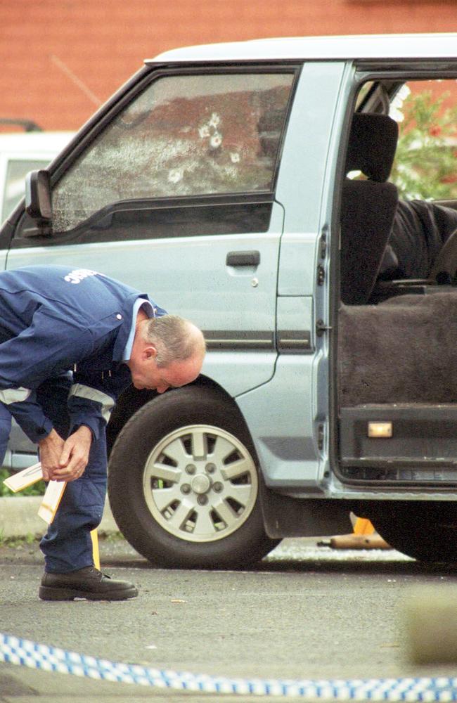 A forensic officer examines a bullet at the scene of the shooting. The discarded shotgun can be seen under the van. Picture: HWT library.