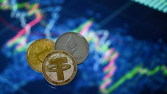 An illustration picture taken in London on May 8, 2022, shows gold plated souvenir cryptocurrency Tether (USDT), Bitcoin and Etherium coins arranged beside a screen displaying a trading chart. - Tether (USDT) is an Ethereum token known as a stablecoin that is pegged to the value of the US dollar, and is currently the largest stablecoin with a market value of USD 83 billion dollars. (Photo by Justin TALLIS / AFP)