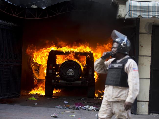 A police officer stands in front of a burning car set alight by protesters in Port-au-Prince, Haiti. Picture: AP Photo