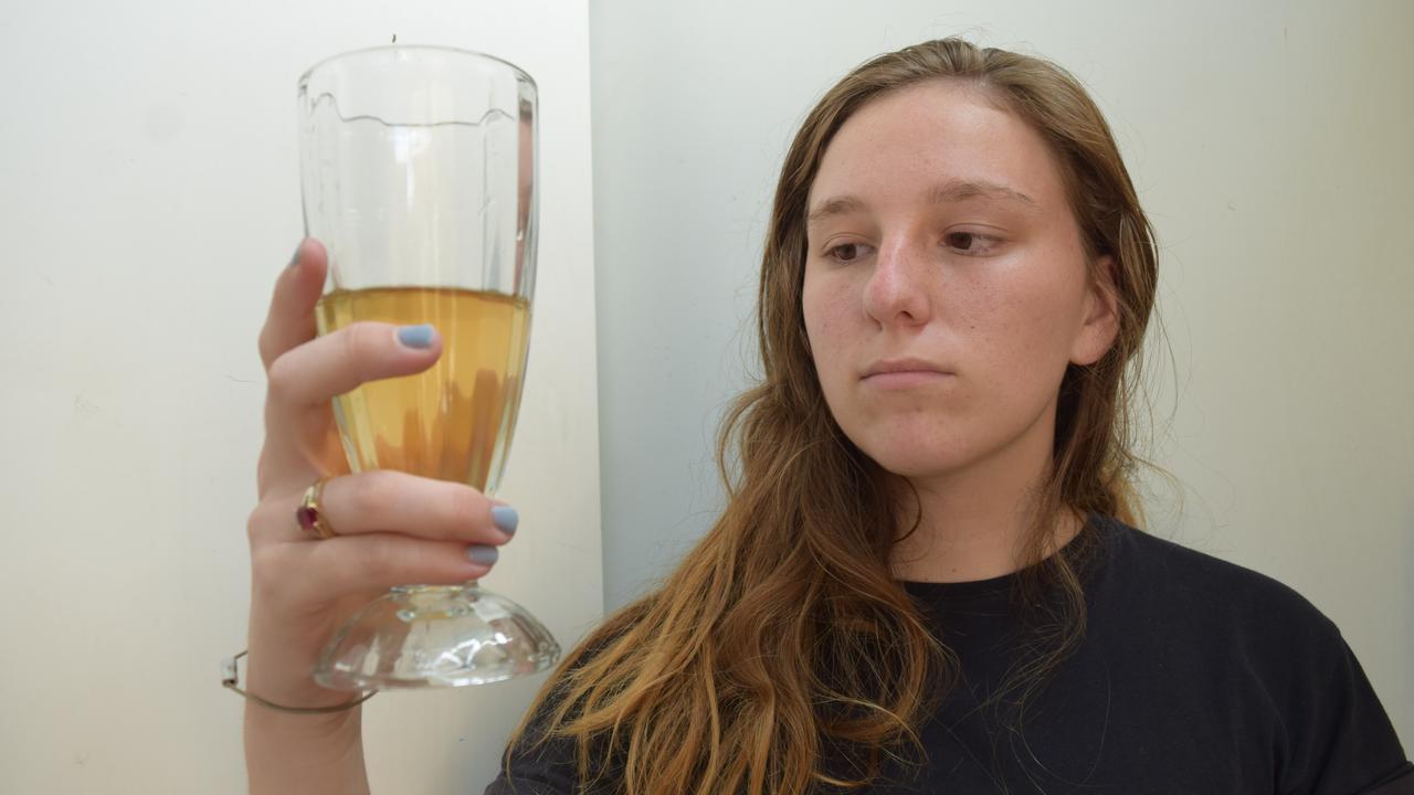Resident Jess Walsh holding a glass of the discoloured water Clermont residents have had to endure for weeks. Photo: Zizi Averill