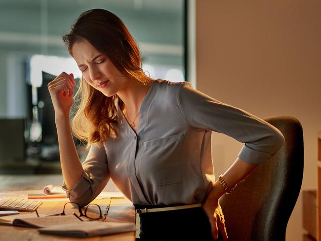 Shot of an attractive young businesswoman holding her back in pain while working late in the office