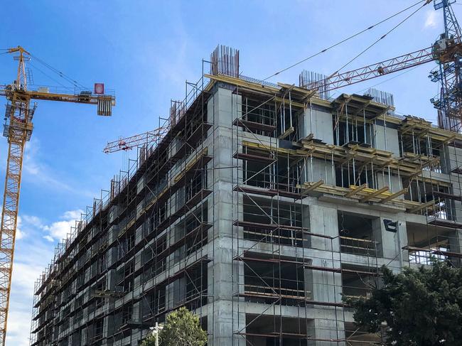 Construction of a monolithic frame house of concrete and gas silicate blocks with lots of scaffolding using a large crane against a blue sky.