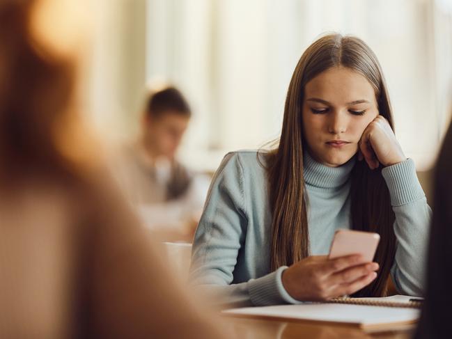 Female students using mobile phone while feeling bored on a class at high school.