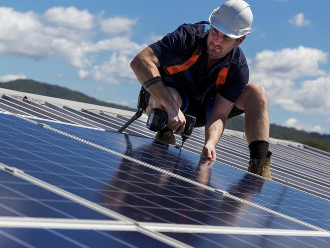 TRADESMAN/ TRADIE/BUILDING INDUSTRY:  Solar panel installer with drill installing solar panels on roof on a sunny day