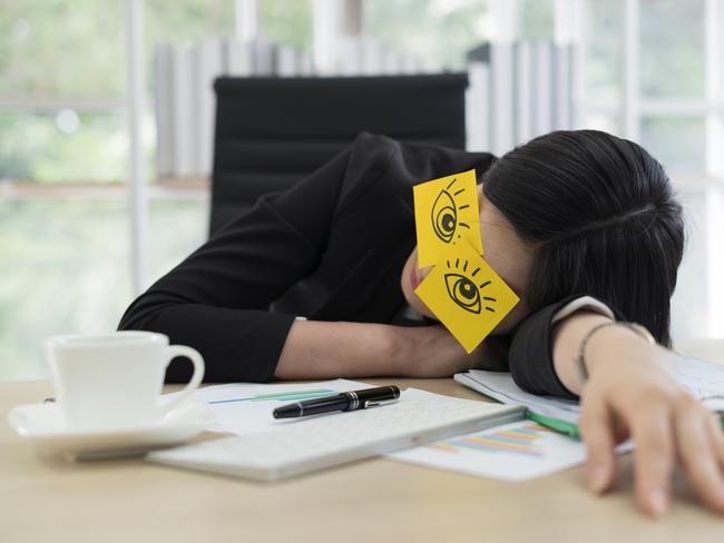 Young business woman with fake eyes painted on adhesive note sleeping at workplace in office