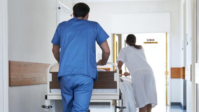 Rearview shot of hospital staff wheeling a patient in a gurney down a corridor