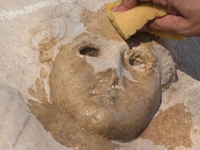 Israel Antiquities Authority (IAA) southern district director Saar Ganor cleans the lid of a unique Roman-era sarcophagus adorned with the carving of a young man at a warehouse in Bet Shemesh on September 3, 2015. The sarcophagus, estimated 1,800 years old with exquisite carvings of Greco-Roman mythological figures, was found, removed and concealed by workers at a construction site in southern Israeli coastal city Ashkelon before the IAA discovered the ancient artefact damaged. AFP PHOTO / MENAHEM KAHANA