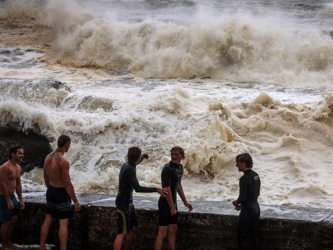 Young men stand behind a wall as they play in record-breaking waves at Coolangatta. Picture: David Gray