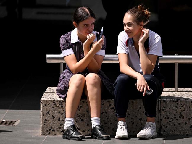 Students look at their phones in Melbourne on November 28, 2024 as Australia looks to ban children under 16 from social media with claims social media platforms have been tarnished by cyberbullying, the spread of illegal content, and election-meddling claims. Australia is among the vanguard of nations trying to clean up social media, and the age limit legislation will make it among the world's strictest measures aimed at children. (Photo by William WEST / AFP)