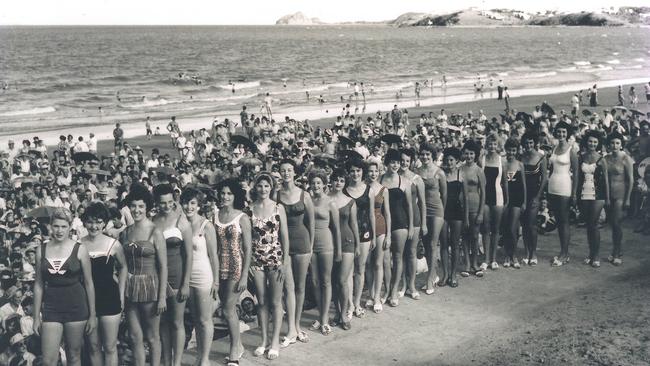 Entrants in a Courier Mail Sungirl Quest at Yeppoon in the mid 1950s. One piece bathers, 23 different styles all with shoulder straps supported by 23 young ladies with smiling faces. Yeppoon Main Beach being a draw card for thousands, most of the visitors arriving by trains from Rockhampton up to five trains some Sundays. Largely undeveloped areas of Cooee Bay/Wreck Point and Rosslyn Bay appear in the background. Modern transport has opened up 18 kilometres of beaches attracting a wide spread of visitors.