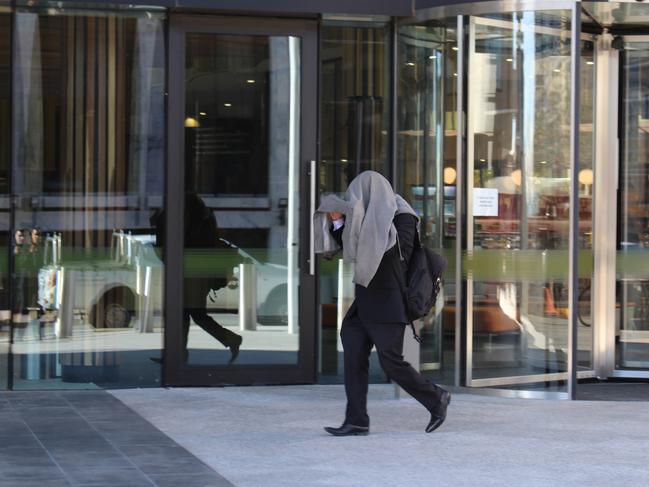 Jason Wayne Conomos covers his face as he leaves court