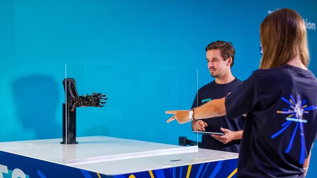 Visitors play rock, scissors, paper against a robotic arm at an Optus 5G demonstration at The Commonwealth Games