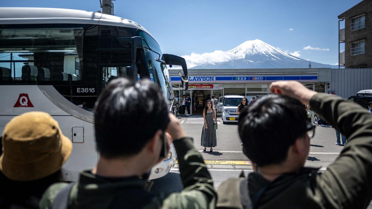 Tourists capture photos of a convenience store and Mount Fuji from across the street in Fujikawaguchiko. A large black barrier is set to be erected here, blocking the iconic view due to authorities’ concerns over crowds of unruly foreign tourists. Picture: Philip Fong/AFP