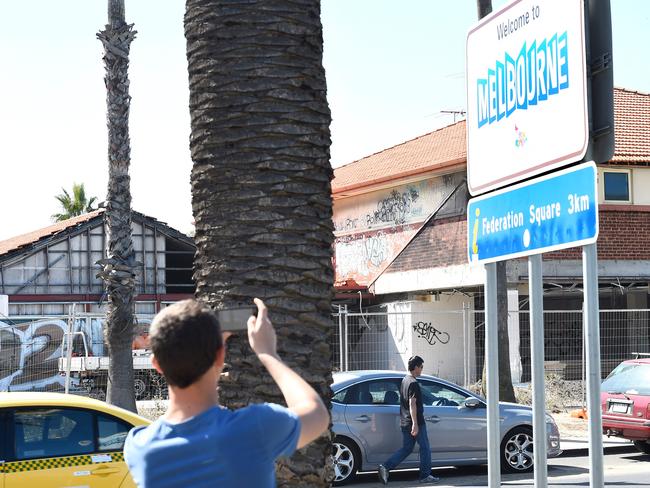 A tourist snaps the “Welcome to Melbourne” sign before the abandoned building. Picture: Mike Keating.