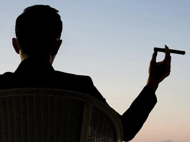 Silhouette of businessman sit on chair and hold a cigar and looking at the city in night.