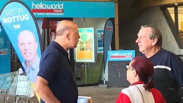 Home Affairs Minister Peter Dutton hands out flyers outside a Helloworld outlet — the same travel agency that has kept the Liberals in the news this week.