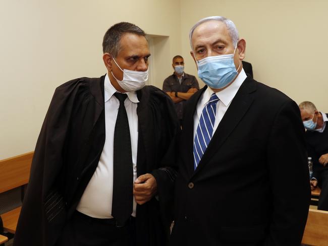 Israeli Prime Minister Benjamin Netanyahu, wearing a face mask in line with public health restrictions due to the coronavirus pandemic, stands inside the court room as his corruption trial opens at the Jerusalem District Court, Sunday, May 24, 2020.  He is the countryÃ¢â¬â¢s first sitting prime minister ever to go on trial, facing charges of fraud, breach of trust, and accepting bribes in a series of corruption cases stemming from ties to wealthy friends. (Ronen Zvulun/ Pool Photo via AP)