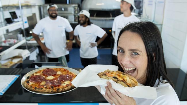 Roma Driscoll tucks into a folded-up pizza at Francesca’s at Glenelg with co-owners Aman Takhar, Nilavan Baskaran and Aiden O'Sullivan. Picture: Mark Brake