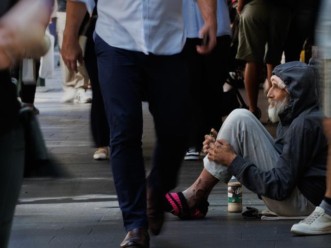 SYDNEY, AUSTRALIA - NewsWire Photos, October 29 2024. GENERIC. Inflation. Shopping. Retail. Economy. Cost of living crisis. Homelessness. Shoppers pass an elderly homeless man with severe wounds / sores on his legs outside a Woolworths in Pitt Street Mall. Picture: NewsWire / Max Mason-Hubers