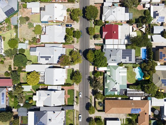 Aerial view of houses and properties in a suburban street in Adelaide's inner northern suburbs: tree-lined with different roof types, varying neatness and with some solar panels evident. Also swimming pools, trampolines, lawns, gardens, driveways.