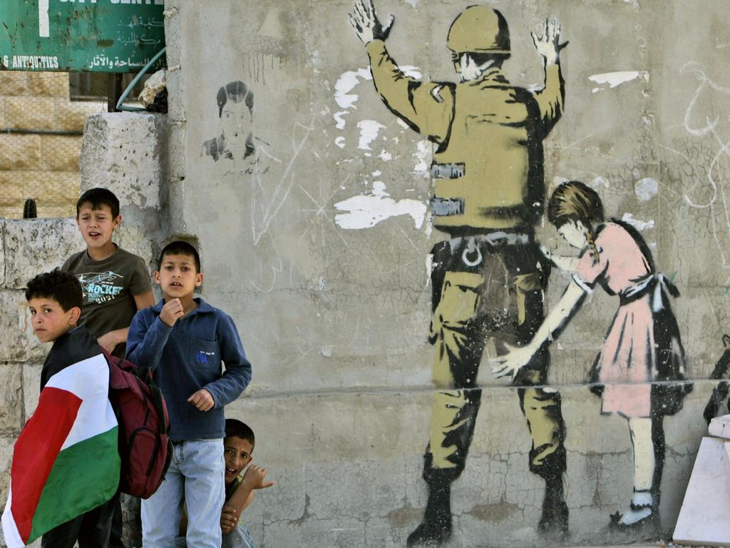 Palestinian youths next to a wall painted by English graffiti artist Banksy in the West Bank city of Bethlehem.