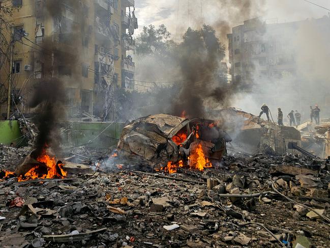 TOPSHOT - A firefighter (C) sprays water on the debris as people gather at the site of an Israeli strike in southern Beirut on March 28, 2025. Israel carried out air strikes in southern Lebanon on March 28 after its defence minister threatened Beirut over new rocket fire, rattling an already fragile truce that largely ended more than a year of hostilities with Hezbollah. (Photo by AFP)