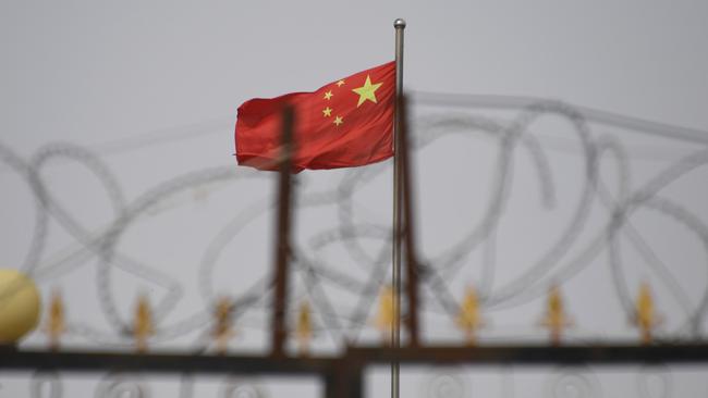 The Chinese flag behind razor wire at a housing compound in Yangisar, south of Kashgar, in China's western Xinjiang region, where the Uighur minority is straitjacketed by surveillance and mass detentions. Picture: AFP