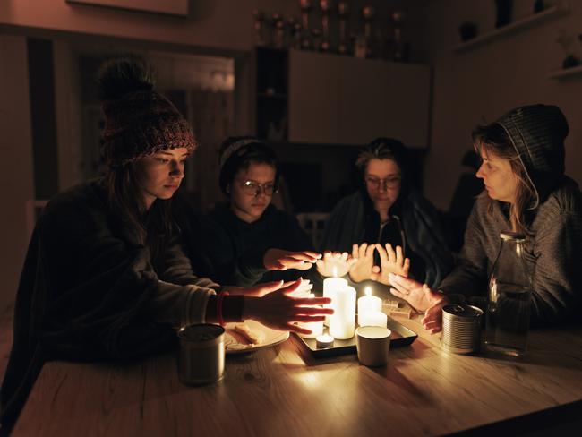 During the energy crisis family is sitting by the table, lit by candles. Everyone is wearing warm clothes because of heating problems during the power outage. They are eating dry biscuits and warming hands from the candle flame. Canon R5 istock image ,