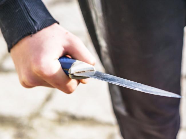 Close-up of a young man's hand with a knife, a big blade. Arrogance and violence among young people. Shallow depth of focus.