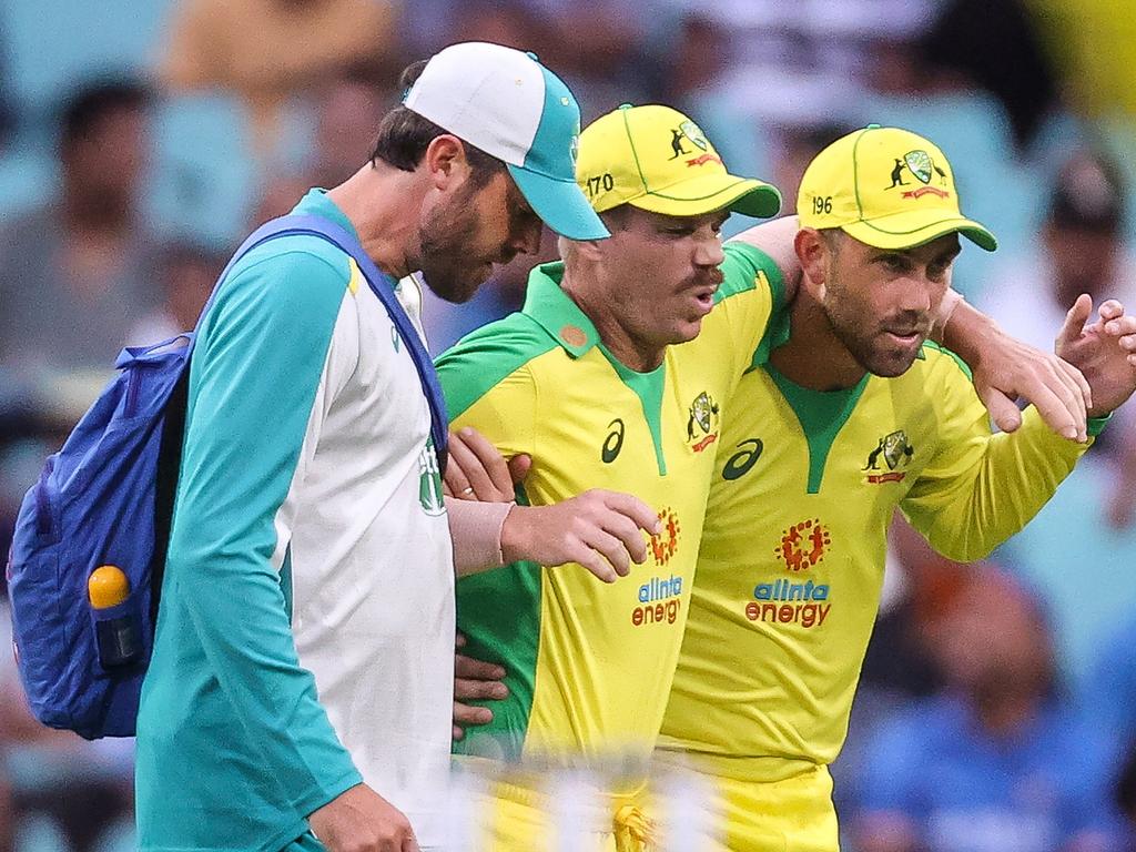 David Warner being assisted by teammate Glenn Maxwell and a trainer as he leaves the field after he suffered a groin injury.