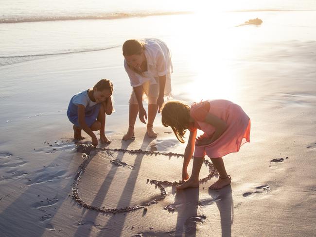 Mother and daughters playing together making heart shapes on a beach at sunset