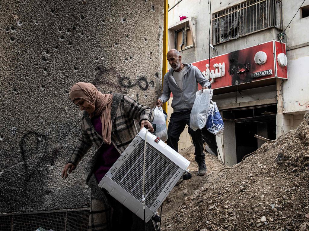 Displaced Palestinians carry personal belongings they retrieved from their home as they walk past a bullet-riddled wall in the Jenin camp for refugees, in the occupied West Bank. Picture: AFP