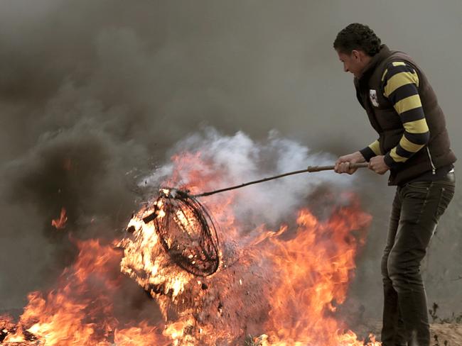 A Palestinian protester burns tires next to Gaza's border with Israel, east of Beit Lahiya, Gaza Strip, Tuesday, April 3, 2018. Israel's defense minister said Tuesday that the military will not change its tough response to Hamas-led mass protests, warning that those who approach the border are putting their lives at risk. Eighteen Palestinians were killed by Israeli fire last Friday, the first day of what Hamas says will be six weeks of intermittent border protests against a stifling blockade of the territory. (AP Photo/Adel Hana)