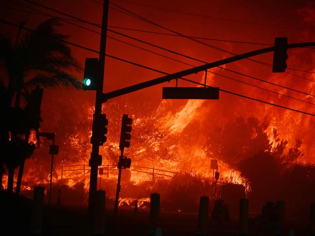 TOPSHOT - Flames overtake the intersection of Temescal Canyon and Pacific Coast Highway Fire at the Palisades Fire in Pacific Palisades California on January 7, 2025. A fast-moving wildfire in a Los Angeles suburb burned buildings and sparked panic, with thousands ordered to evacuate January 7, 2025 as "life threatening" winds whipped the region. Frightened residents abandoned their cars on one of the only roads in and out of the upscale Pacific Palisades area, fleeing on foot from the 770-acre (310-hectare) blaze engulfing an area crammed with multi-million dollar homes in the Santa Monica Mountains. (Photo by Robyn Beck / AFP)