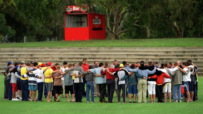 Teammates link arms in a circle during a minute's silence around the spot where footballer Jake Watson collapsed after on-field collision during a SANFL under 19s football match between West Adelaide and Woodville-West Torrens at Richmond Oval in 2002. Jake later died in hospital.