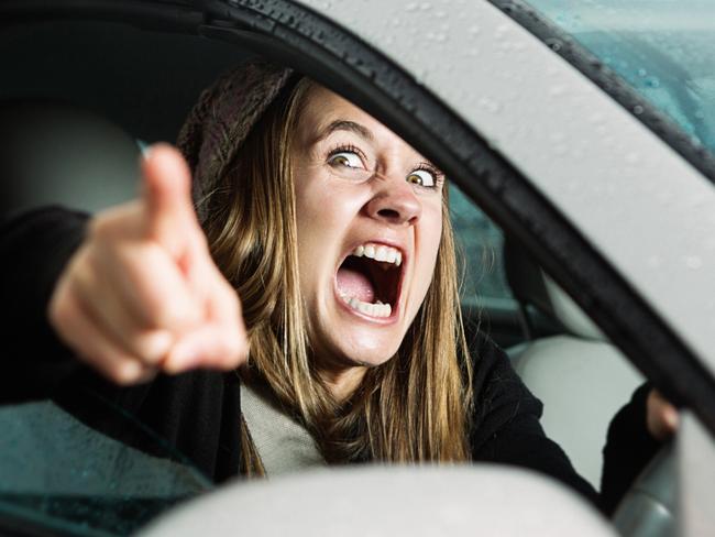 A young woman yells and points at something or someone in a fit of road rage, seen through her car window.