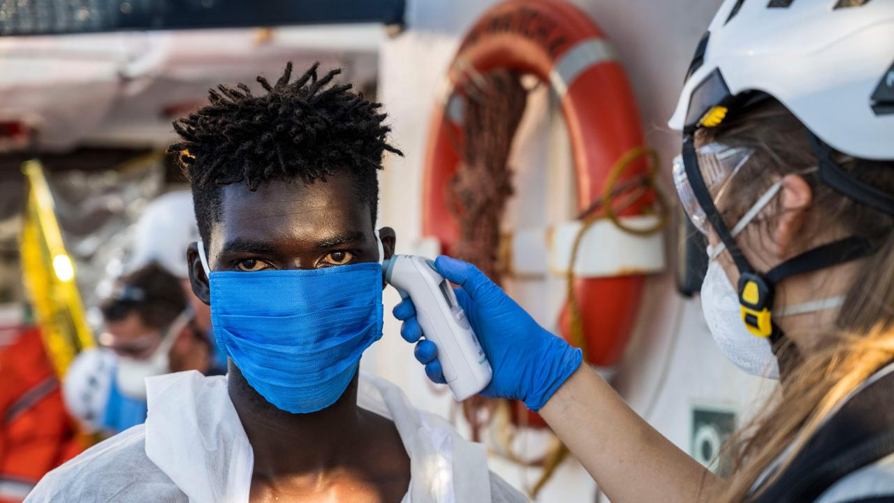 A crew member of the civil sea rescue ship Sea-Watch 4 takes the temperature of a migrant wearing a protective face mask who was just helped off the rescue ship. Picture: Thomas Lohnes / AFP