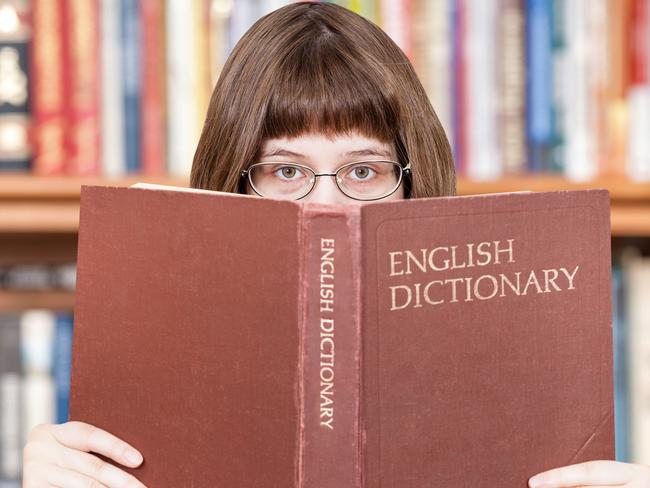 girl with spectacles looks over English Dictionary book and bookcase on background