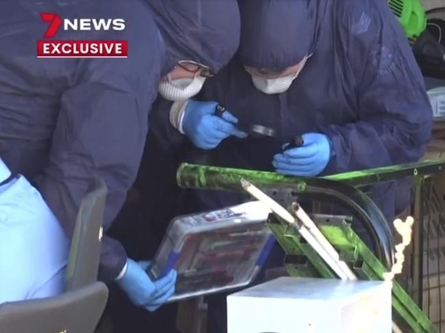 Forensic officers examine a container full of pens and pencils.