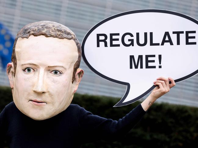 An activist of environmental NGO Avaaz wearing a mask depicting Facebook CEO Mark Zuckerberg holds a banner reading "Regulate me" during an action marking the release of the Digital Services Act, outside the European Commission building in Brussels on December 15, 2020. - The European Union on December 15, 2020 will unveil tough draft rules targeting tech giants like Google, Amazon and Facebook, whose power Brussels sees as a threat to competition and even democracy. (Photo by Kenzo TRIBOUILLARD / AFP)