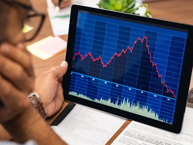 Closeup of a stock market broker working with graphs on digital tablet at office. Rear view of stock agent reading bad report and graph. Back view of multiethnic businessman analyzing fall sales.