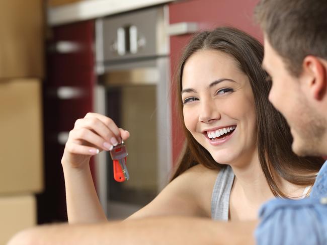 Happy new flat couple of owners showing keys sitting in the floor of the kitchen while moving home