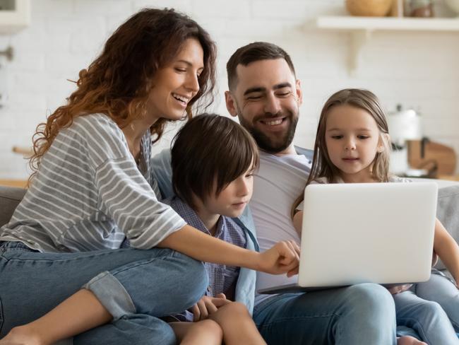 Happy young family with little kids sit on sofa in kitchen have fun using modern laptop together, smiling parents rest on couch enjoy weekend with small children laugh watch video on computer at home