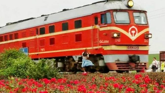 ONLINE ONLY - FEE APPLIES Pic shows: The victim (white top, blue skirt) taking photos with a train. A teenage girl in China has died after being hit by a train while she posed for a selfie. The girl is said to have stood dangerously close to the tracks while she photographed herself in a springtime scenery, ignoring warnings from other tourists to stand clear of potential trains. The 19-year-old, who was unnamed in reports, can be seen in photos of the scene in Foshan, a city in South Chinaâ€™s Guangdong Province, as she holds out her mobile phone in front of herself to take the perfect selfie. Dressed in a white top and blue skirt, the girl was reportedly drawn to that particular stretch of rail by a sea of roses growing nearby, which also attracted hundreds of others. The victim, however, took her picture project one step further by straying too close to the railway tracks, and on more than one occasion let blaring locomotives pass near her until she was finally struck by a freight train. As can be seen from the photograph, the girlâ€™s lifeless body was flung to one side of the tracks following the fatal accident. Reports citing witnesses said that bystanders had actively asked the girl to keep a safe distance from the tracks. But the victim ignored all warnings. Arriving paramedics are said to have pronounced the girl dead at the scene, while this latest incident may give local officials a reason to restrict visitor access to the popular scenic train tracks. Officials in Beijing have already barred visitors from a mountainous tourist spot â€“ which also has a railway track running through it â€“ after hundreds of unruly photographers strayed onto the tracks and caused a number of delays. While selfies may never be listed as an official cause of death, there have been an increasing number of selfie-related deaths in China in recent years, including those of victims who tried to take the perfect photo while perched atop dangerous cliffs and waterfalls. (ends) Picture: CEN/Australscope