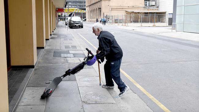 John Mete 80 from Victoria, tries to pick up an eScooter on an Adelaide footpath that was blocking the footpath pushing him on the road. The ebike was too heavy for him and when the eScooter alarm went off so he stopped moving it. Picture: Tricia Watkinson